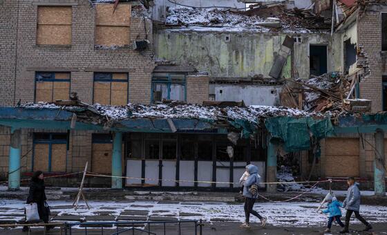 Прохожие на фоне разрушенного войной здания, Украина.